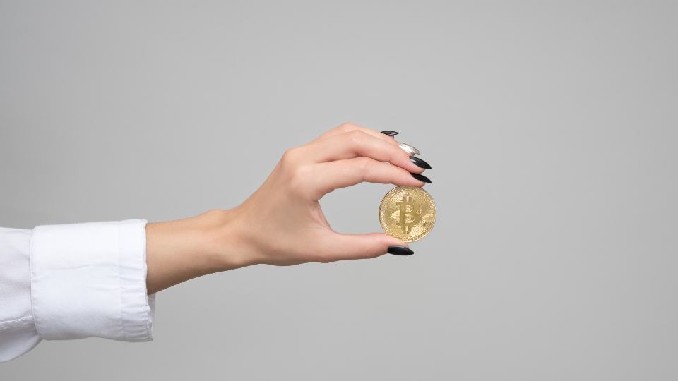 A hand holding a gold bitcoin coin between two fingers